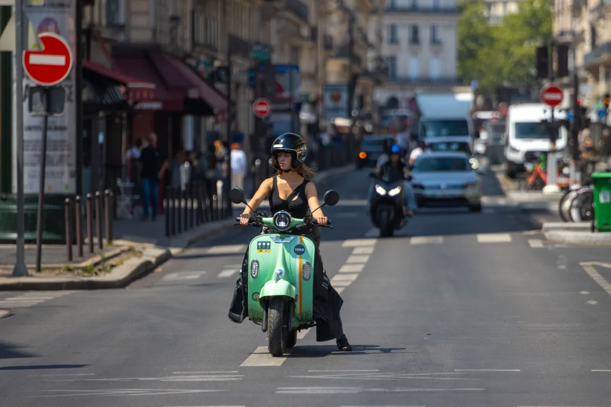 A woman rides a scooter through the busy streets of Paris, France.