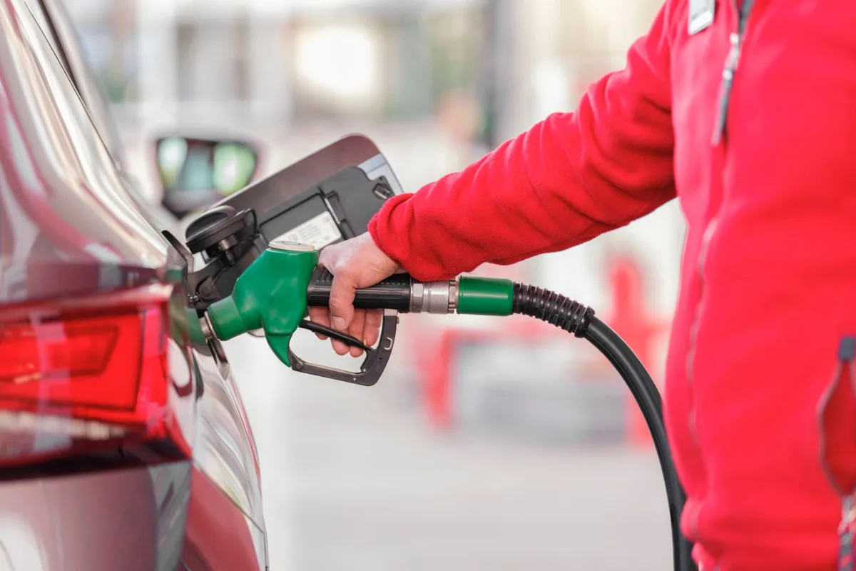 Close-up of a person refueling a car with a green hose at a gas station.