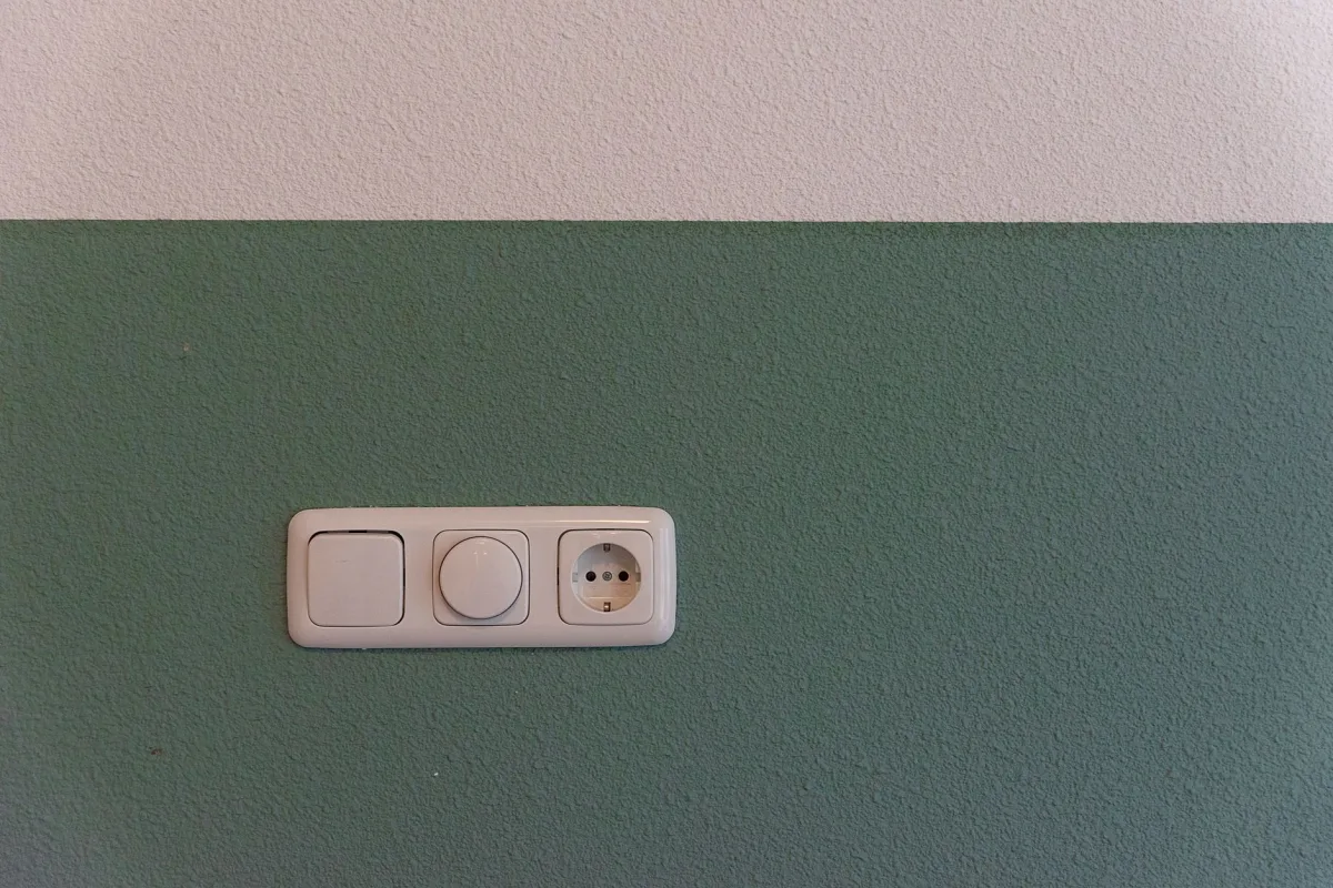 Close-up of a power outlet and switch on a textured green wall indoors.