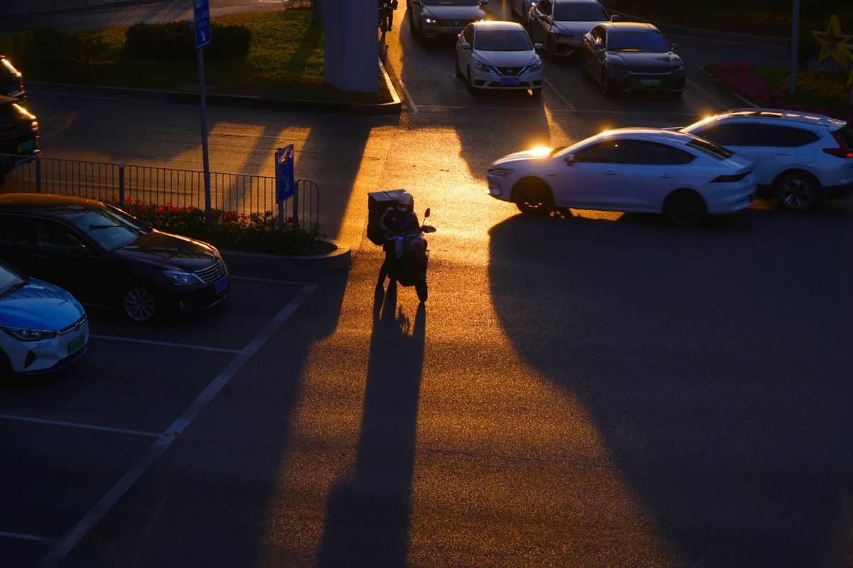 Silhouette of a delivery scooter in city streets during sunset, casting long shadows.