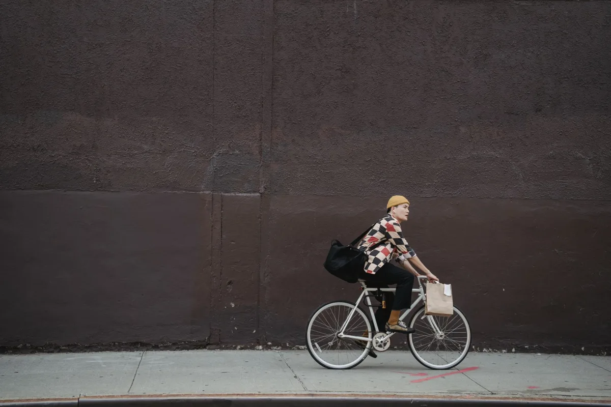 A courier riding a bicycle with bags along a city street against a concrete wall.